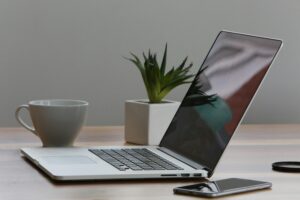 Laptop, phone, cup, and plant on desk.
